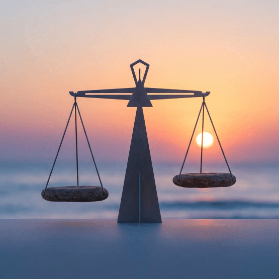 Metal scales with stone pans perfectly balanced against a coastal sunset background.