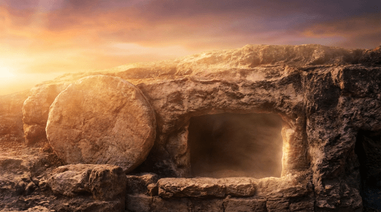 An empty stone tomb with its circular entrance stone rolled to the side at sunrise.