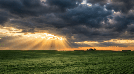 Sunbeams breaking through dark storm clouds over rolling green hills and a distant farmhouse.