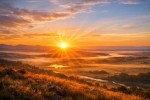 Sun rising over a mist-covered valley with winding river and distant mountains