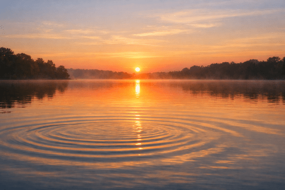 Sunrise over calm lake with mist and concentric ripples on water