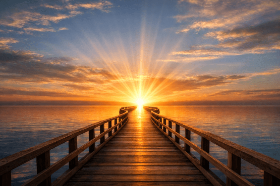 Wooden pier extending over calm water with sun setting at horizon