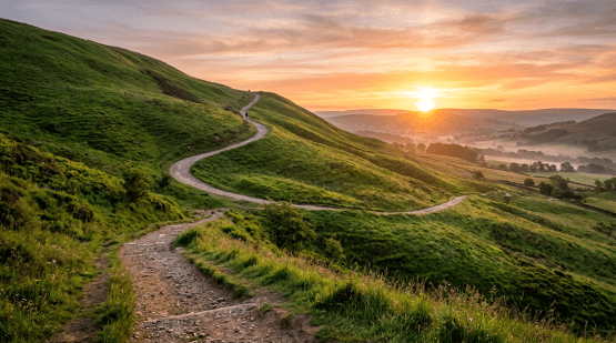 Winding gravel trail on green hills with sunset in background
