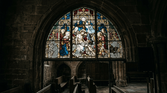 Stained glass window portraying a biblical scene with figures around Jesus in a historic stone church interior
