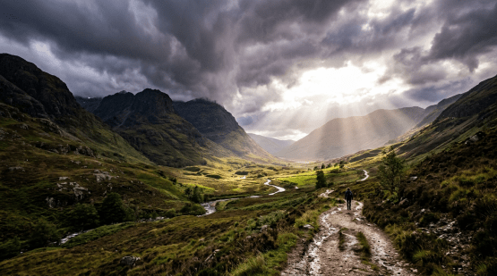 Hiker walking on a winding trail through a green valley with sun rays breaking through cloudy sky